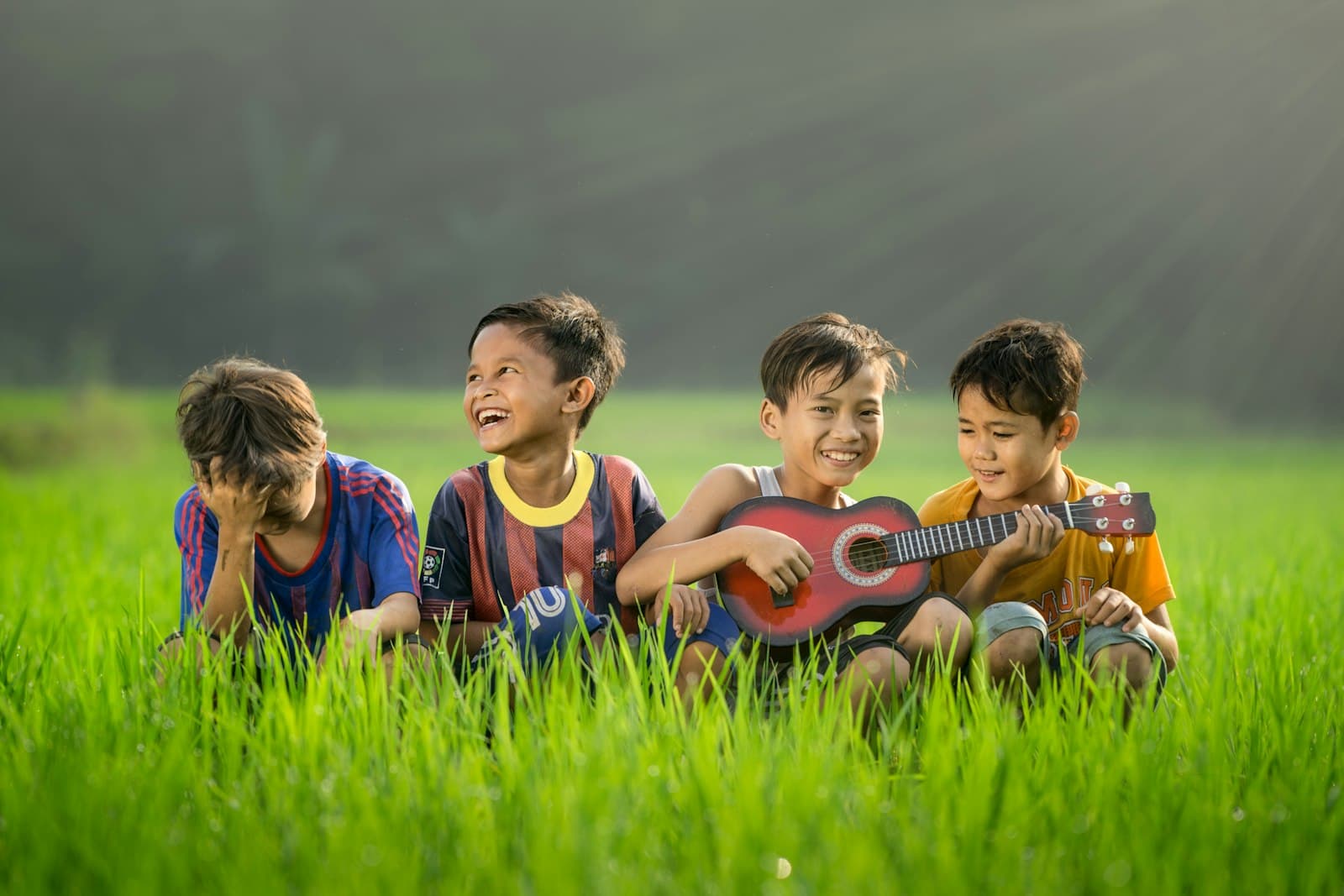 Niños riendo en un campo verde mientras uno de ellos toca una pequeña guitarra