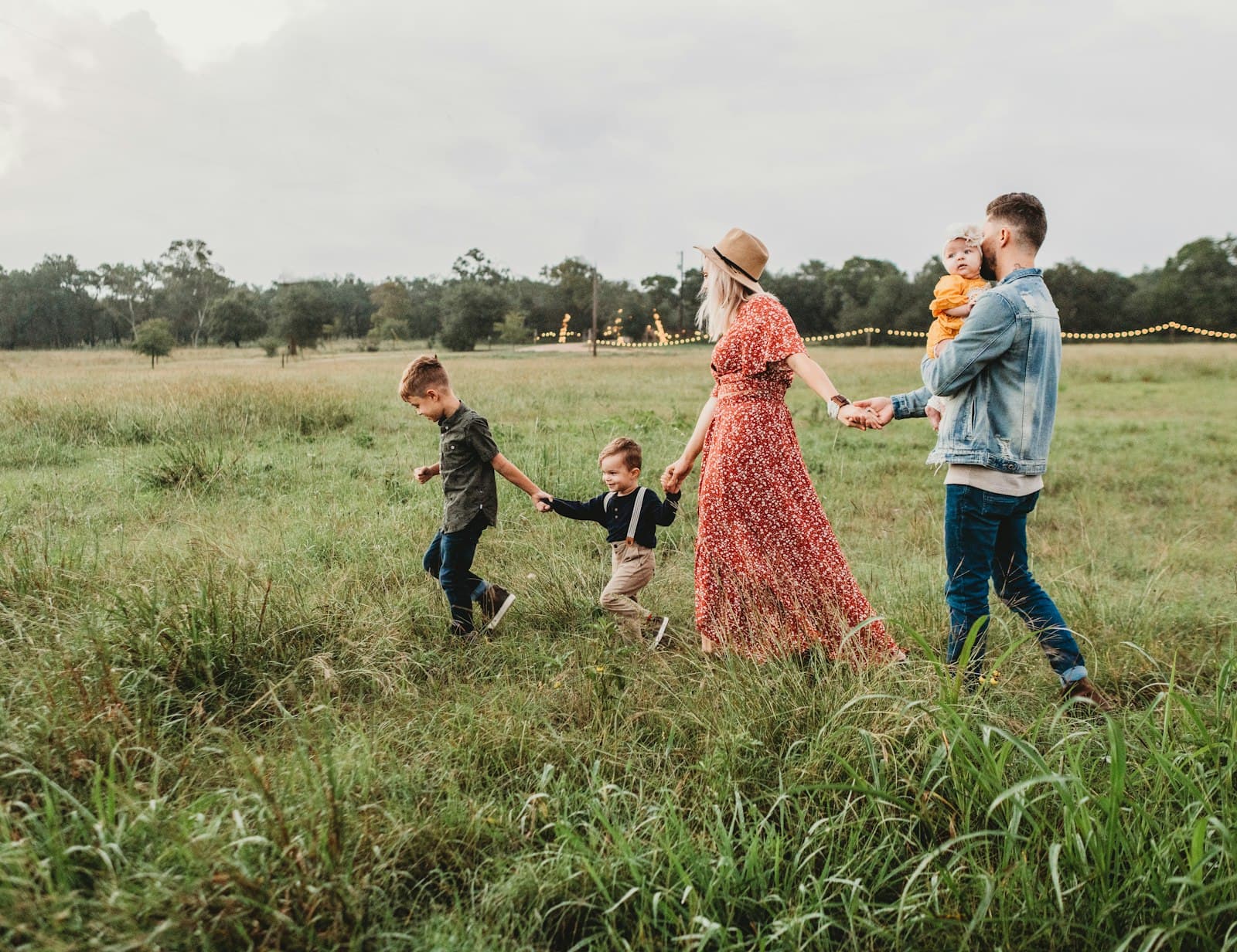 Padres con sus tres hijos caminando de la mano por un campo verde