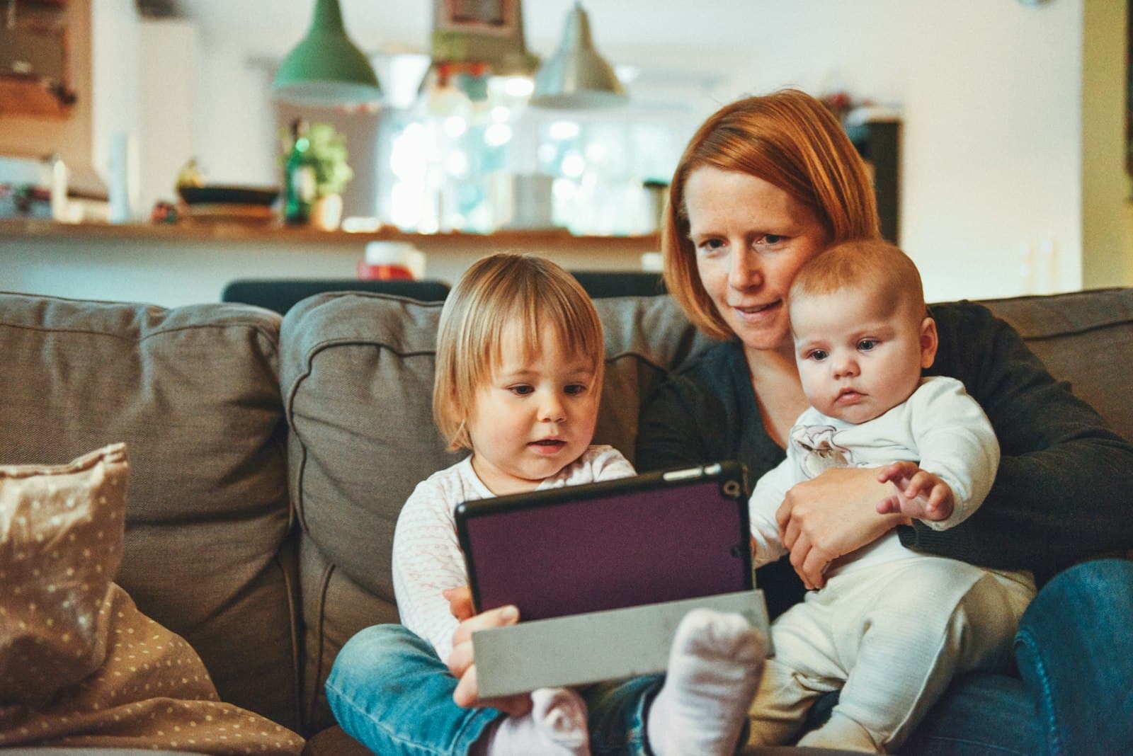 Madre en el sofá con sus dos hijos pequeños viendo juntos un video en una tablet