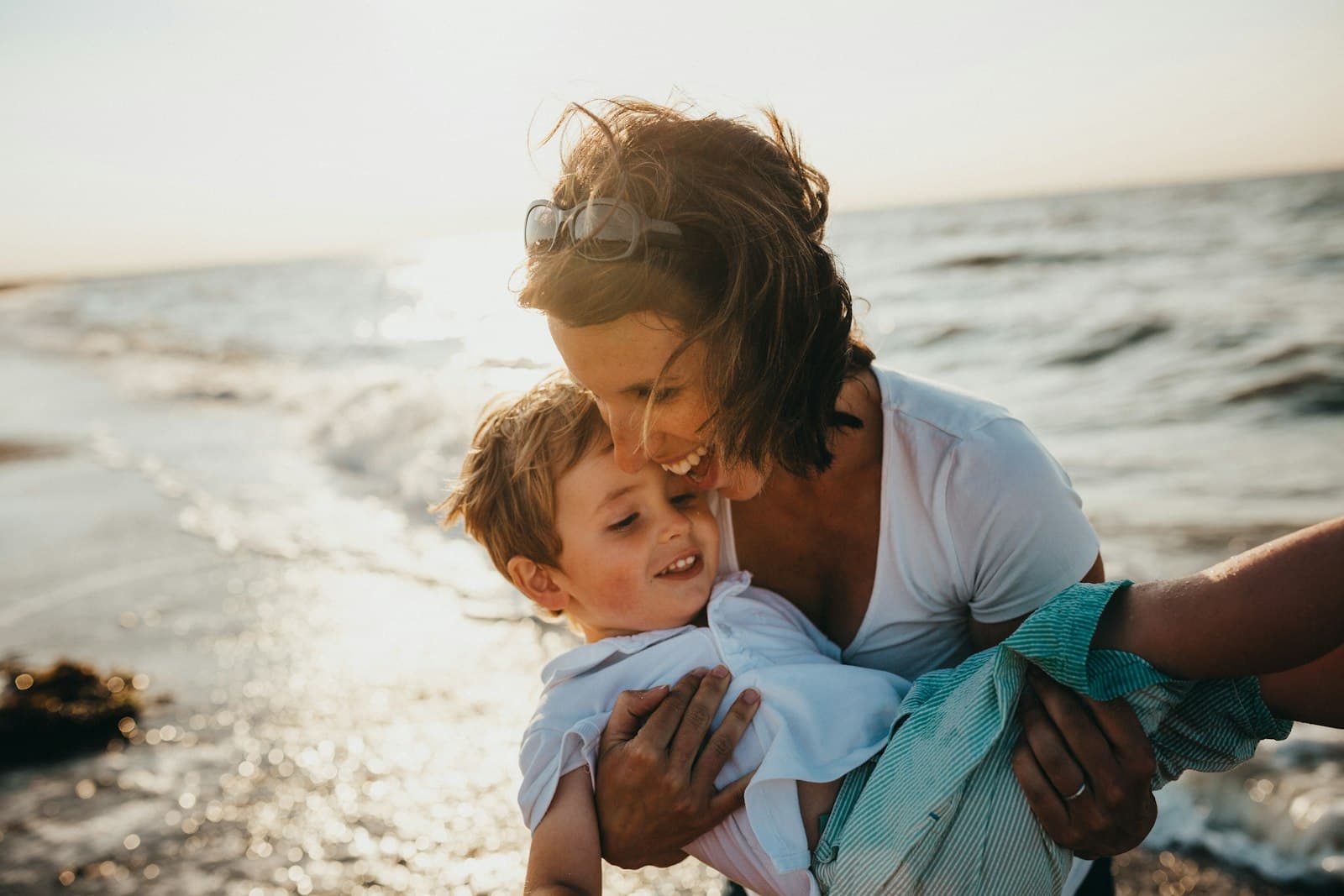 Madre abrazando a su hijo pequeño en la orilla de la playa bajo la luz dorada del atardecer